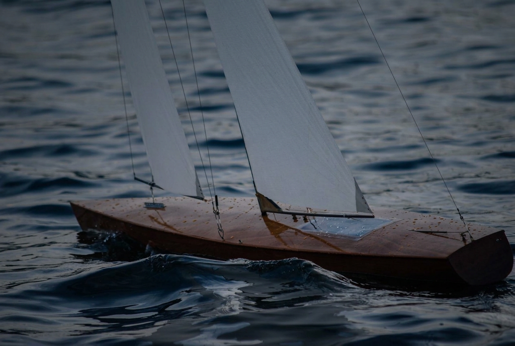 A small wooden sailboat with white sails floating on dark blue water.