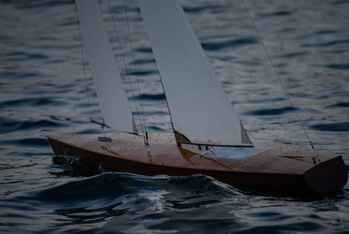 A small wooden sailboat with white sails floating on dark blue water.