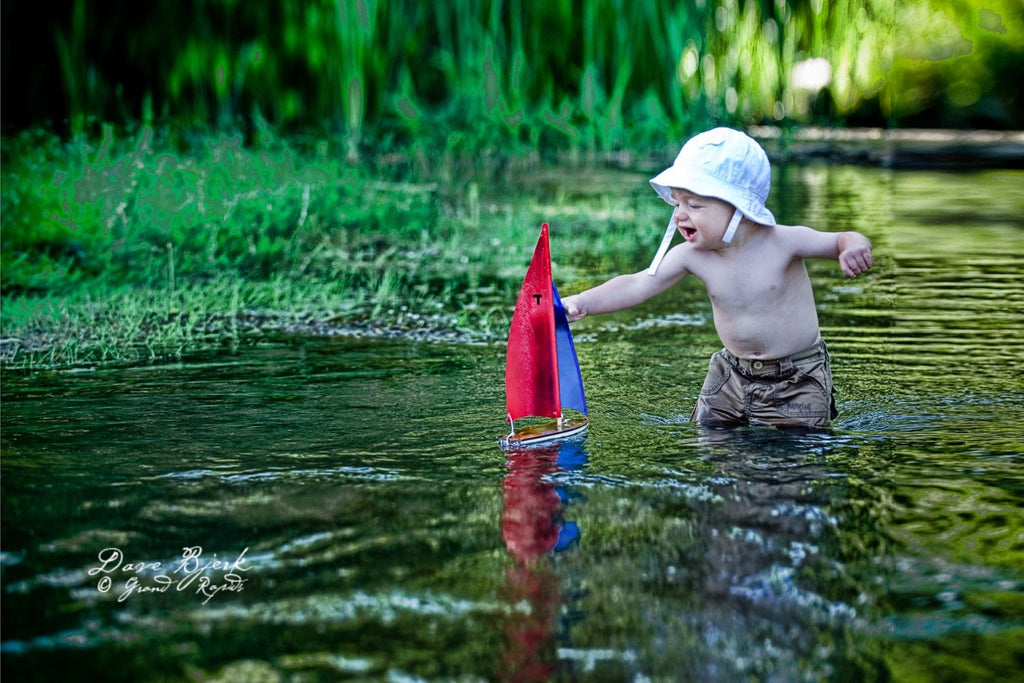Wooden Toy Sailboat enjoyed by a small child in a pond