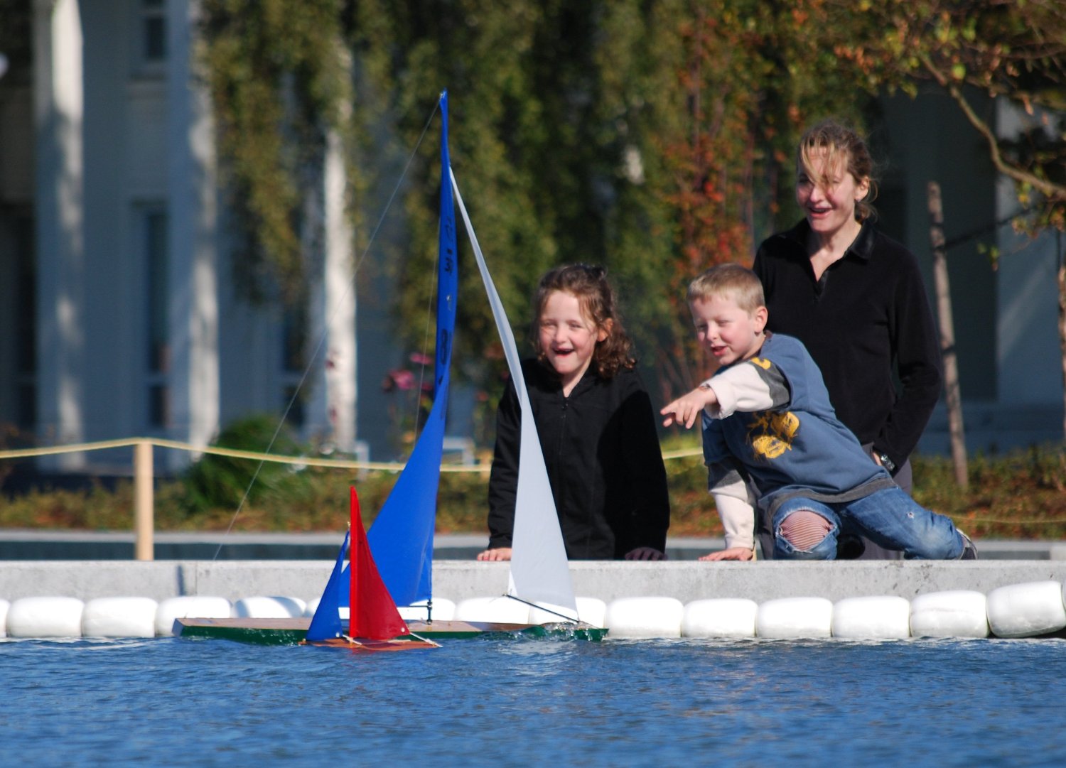 Children impressed by 12 inch Wooden Toy Sailboat sailing beside an RC Sailboat